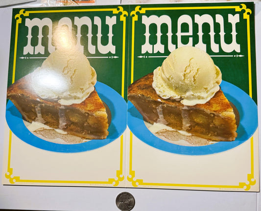 Two vintage mint-green ice cream menu boards with yellow borders showing pie slices topped with scoops, displayed next to a p