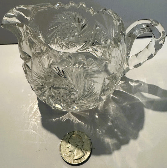 Clear cut glass creamer with pinwheel and hobstar patterns, displayed next to a 1982 quarter for scale