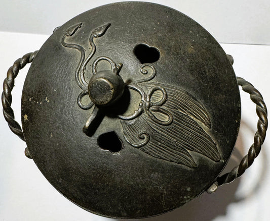 Top view of bronze censer lid with twisted handles, decorative scrollwork, central knob, and embossed bird design with detail