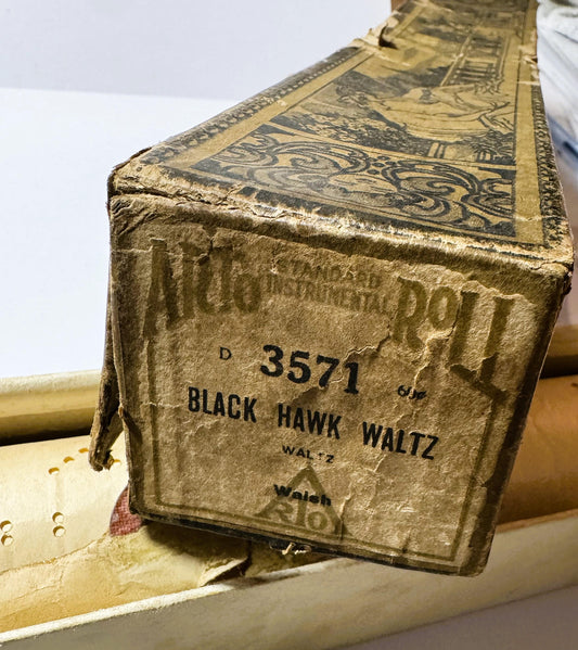 Closeup of vintage player piano roll box showing embossed gold cover with "Black Hawk Waltz" and number "3571" printed in bla