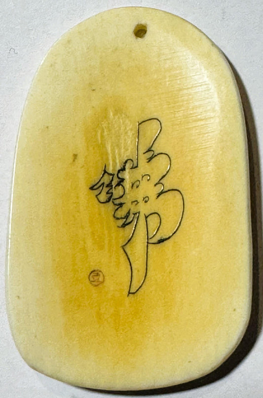 Pale yellow ox horn pendant with engraved line drawing of Budai figure, shown from front against white background with small