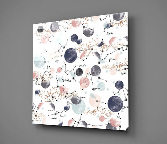 Angled perspective of glass wall art displaying zodiac constellations with watercolor moons in navy, pink, and blue tones on white background.