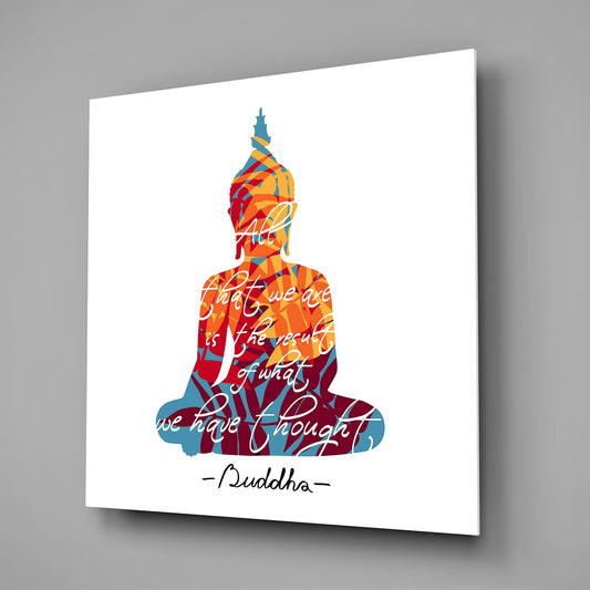 Angled view of a glass wall art panel displaying a colorful Buddha silhouette in red, orange, and blue with overlaid inspirational text and artist signature.