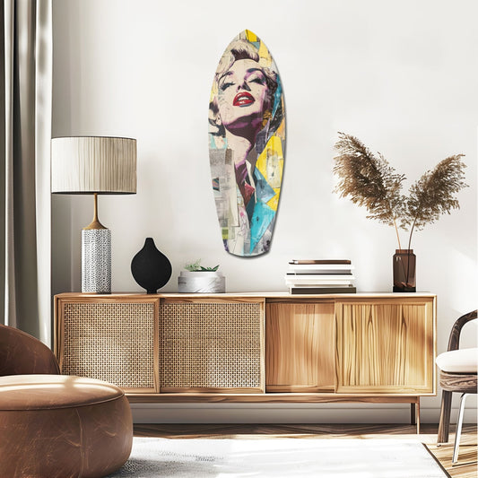 Colorful pop art surfboard featuring blonde woman's portrait in yellow, blue, and purple tones displayed on white wall above wooden credenza.