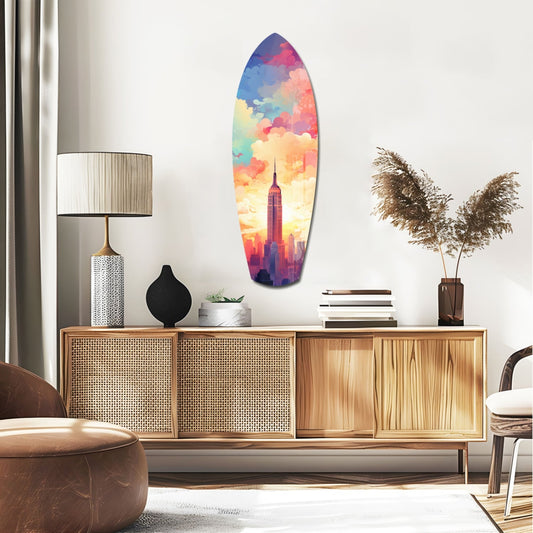 Colorful surfboard-shaped glass wall art depicting Empire State Building silhouette against vibrant rainbow sky, displayed above mid-century wooden credenza in modern living room.