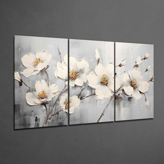 Three-panel glass wall art displaying white blossoms with golden centers on gray textured background, hung on dark gray wall.