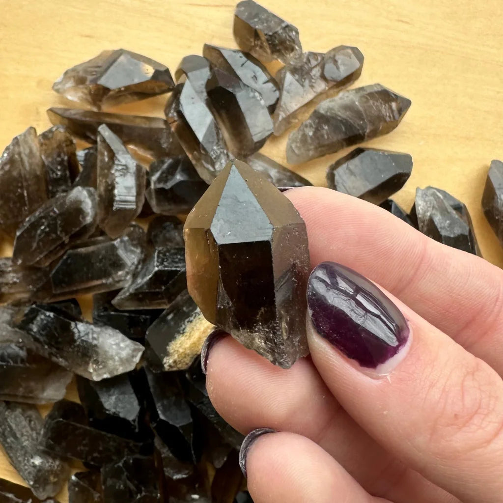 Hand holding natural smoky quartz point crystal with dark inclusions
