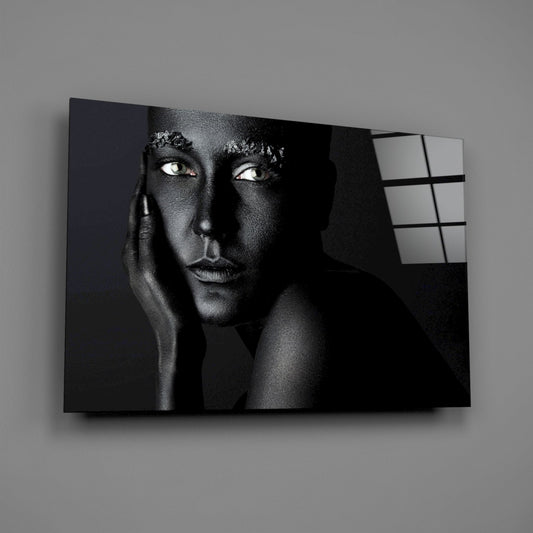 Black and white portrait of a woman with striking eyes on glass wall art, displayed at an angle against a gray wall.