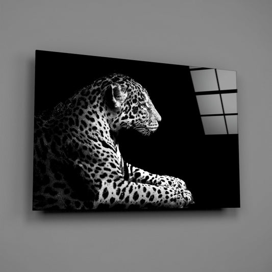 Black and white glass wall art depicting a resting leopard in side profile against dark background, displayed at an angle showing the glass panel edge.