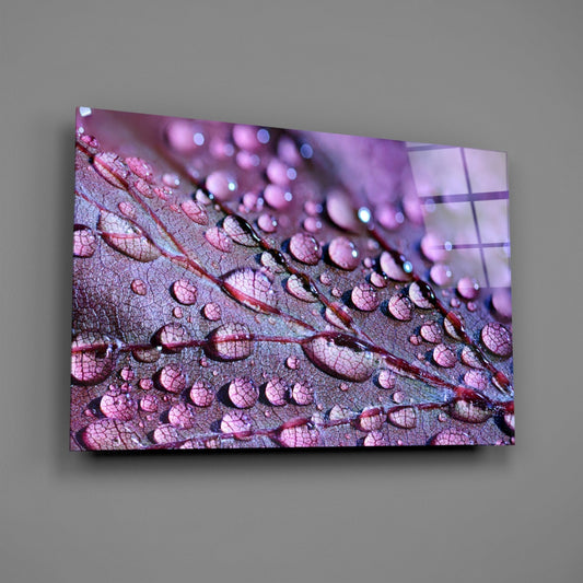 Glass wall art panel displayed at an angle showing violet dew drops on a leaf with red veins and blurred background bokeh.