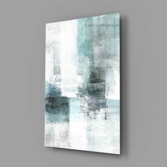 Angled view of a glass wall art panel displaying teal, white, and gray abstract brushstrokes and textured blocks against a gray background.