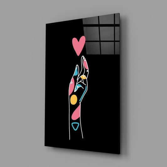 Black glass wall panel displaying colorful line art hand with pink heart above, viewed at angle showing depth and shadow.