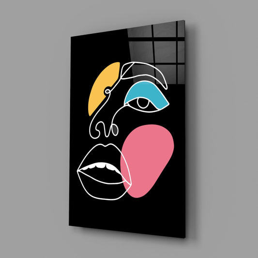Modern glass wall art featuring abstract line-drawn face with yellow, blue, and pink colored shapes on black background, displayed at an angle.