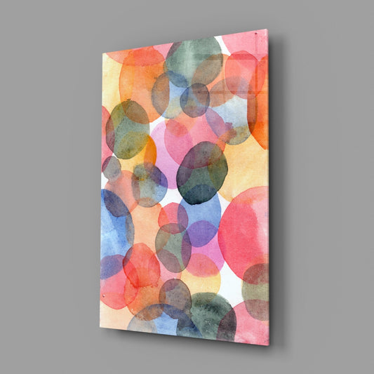 Angled view of rectangular glass wall art displaying overlapping watercolor circles in pink, orange, blue, yellow, and green on white background.