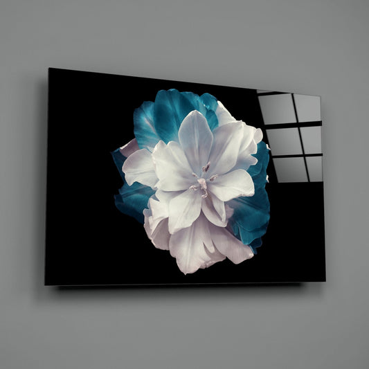 White and teal layered flower glass wall art displayed at an angle against a gray wall, showing the glass panel's edge and reflection.