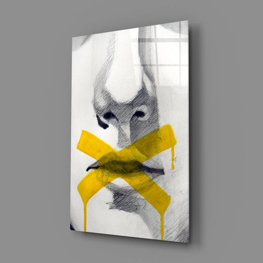 Glass wall art displaying a sketched face with closed eyes and yellow tape crossed over the mouth, mounted at an angle against gray background.