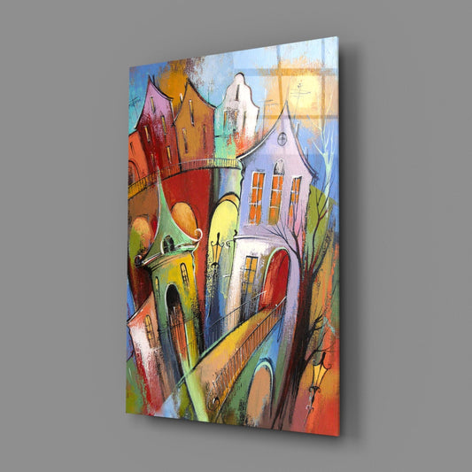 Angled view of glass wall art depicting colorful tilted buildings with steeple and warm yellow sun against gray background.