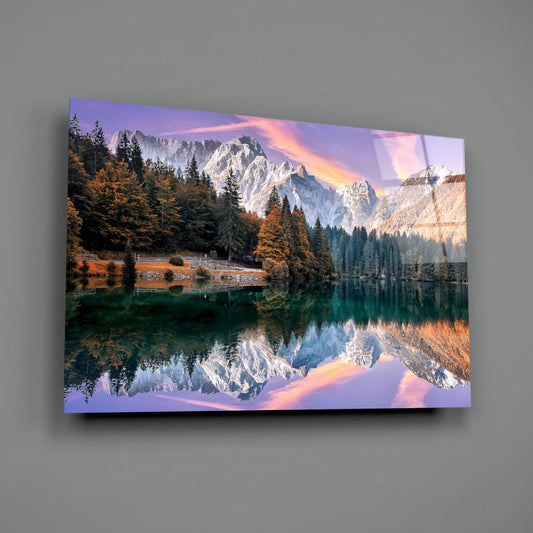 Glass wall art mounted on gray wall displaying snow-capped mountain reflected in emerald lake surrounded by golden autumn forest at sunset.