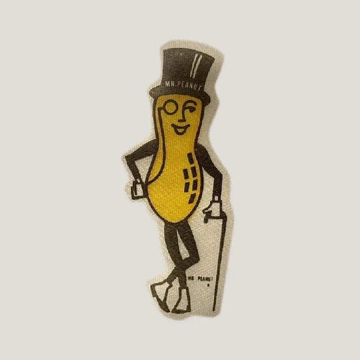 Vintage cloth sticker of yellow Mr. Peanut mascot wearing black top hat with cane.