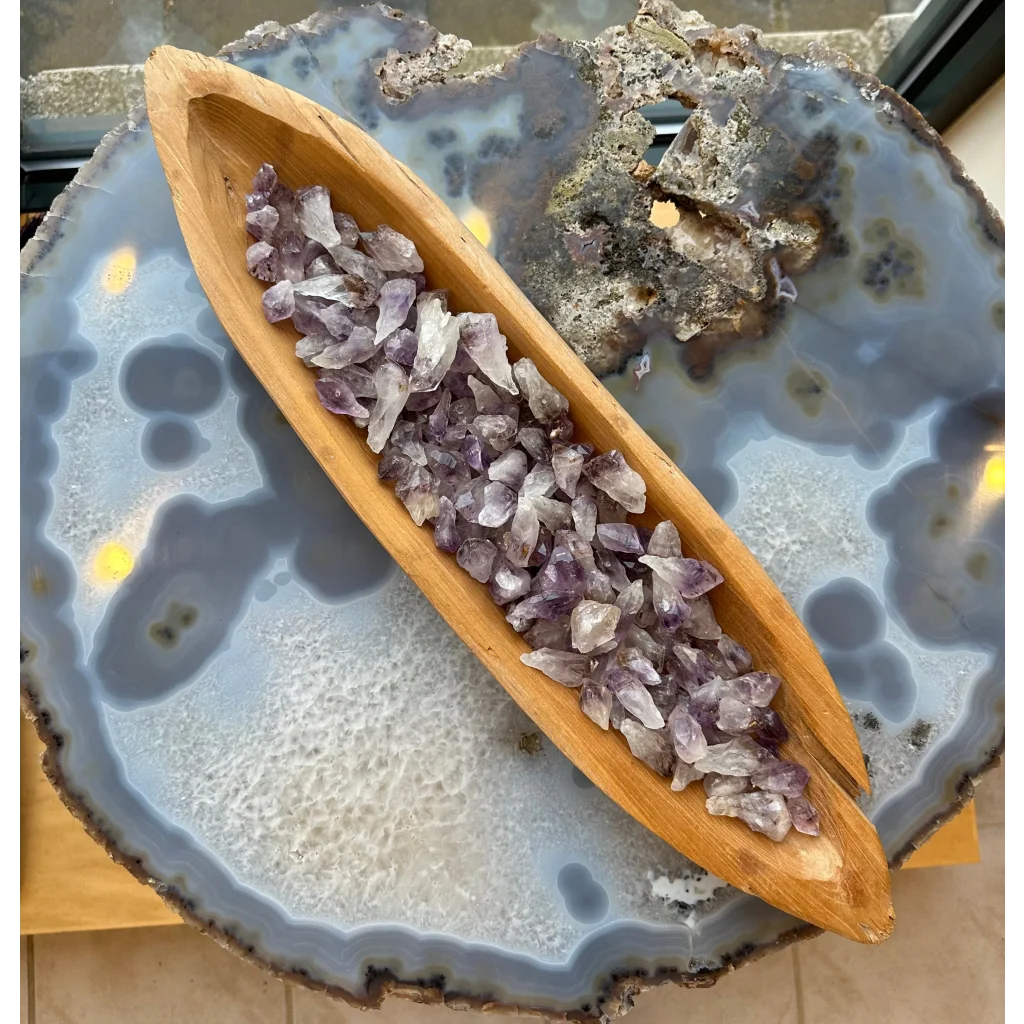 Raw amethyst crystals in wooden boat bowl on agate slab