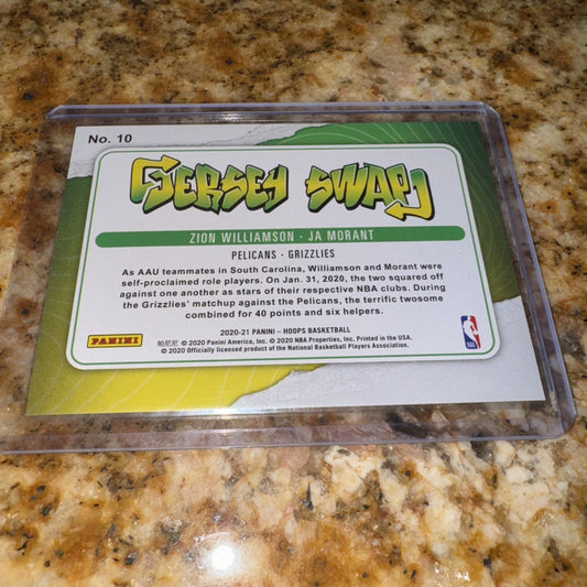 Reverse side of trading card showing "Jersey Swap" title and descriptive text about Williamson and Morant, laid on granite countertop.