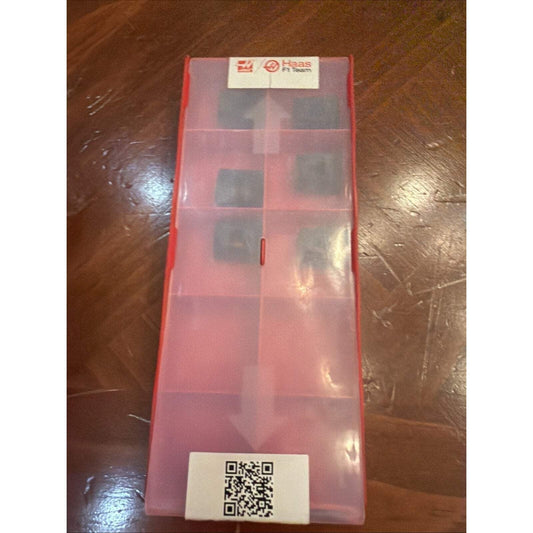 Red plastic storage case with compartmented insert displaying six gray carbide inserts, QR code label at bottom, Haas logo at top.