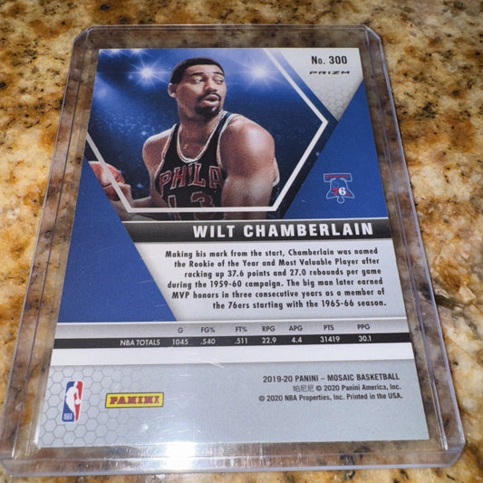 Trading card in clear plastic case displaying Wilt Chamberlain in 76ers uniform on blue background with statistics and text visible.