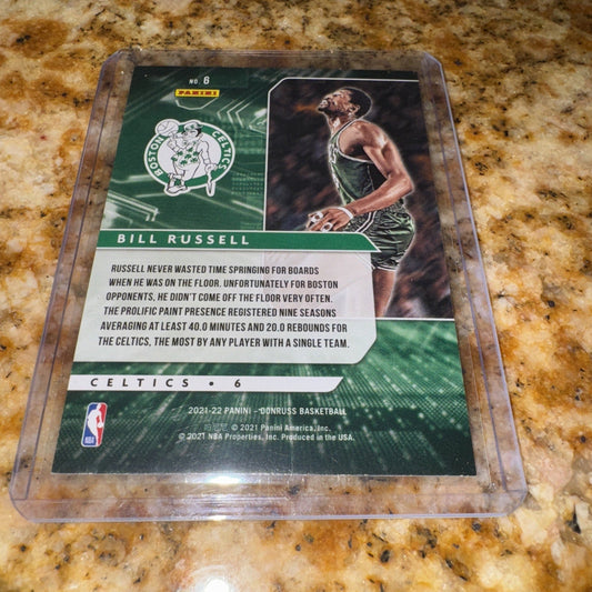 2021-22 Panini Donruss Bill Russell card in clear plastic case on granite countertop, showing green Celtics design with player photo and biographical text.