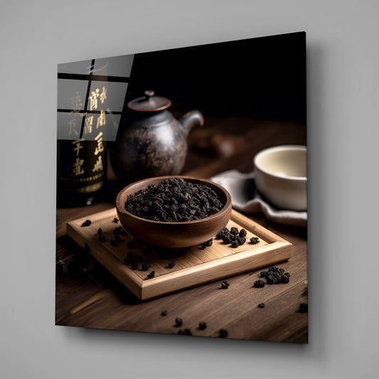 Dark oolong tea leaves in wooden bowl on tray with black teapot and white cup on wooden surface.