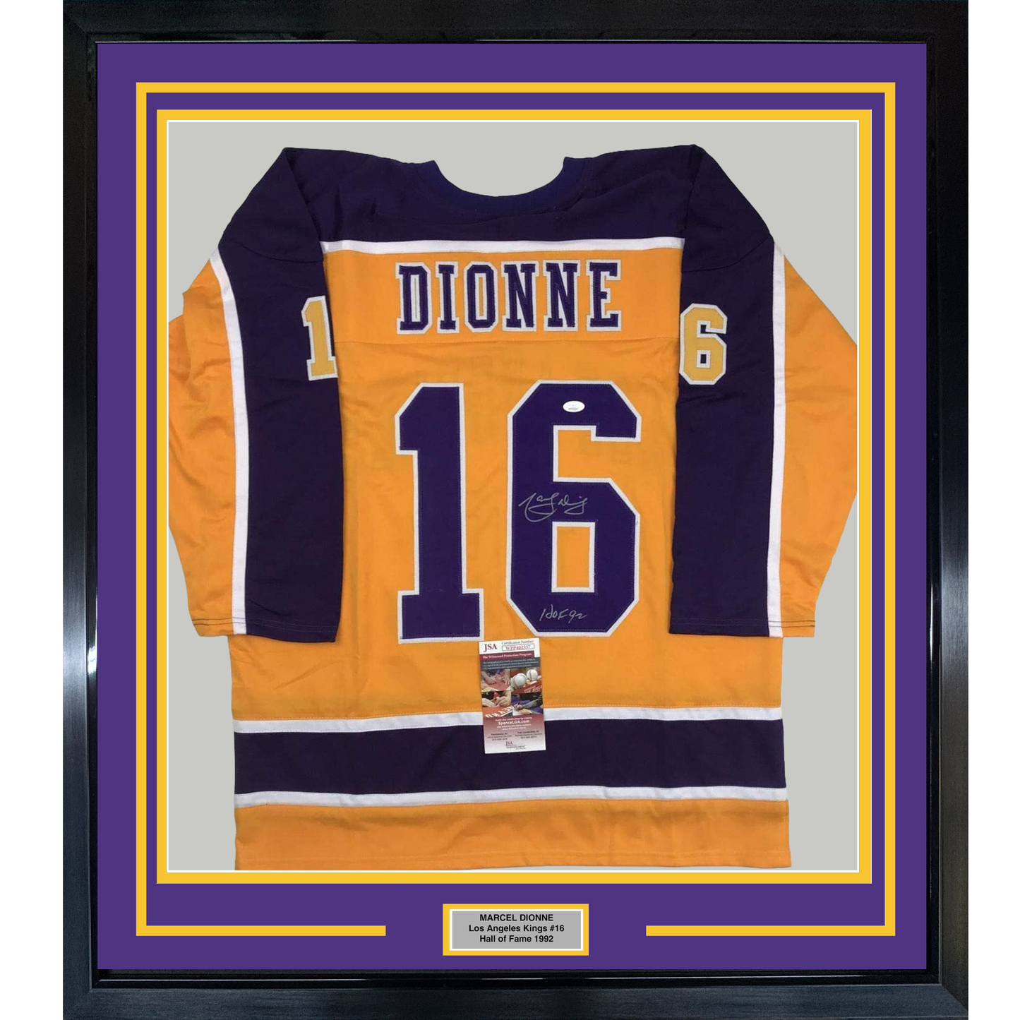 Framed orange and navy Los Angeles Kings hockey jersey #16 with "DIONNE" nameplate, signed, displayed flat against purple and gold matting with authentication certificate.