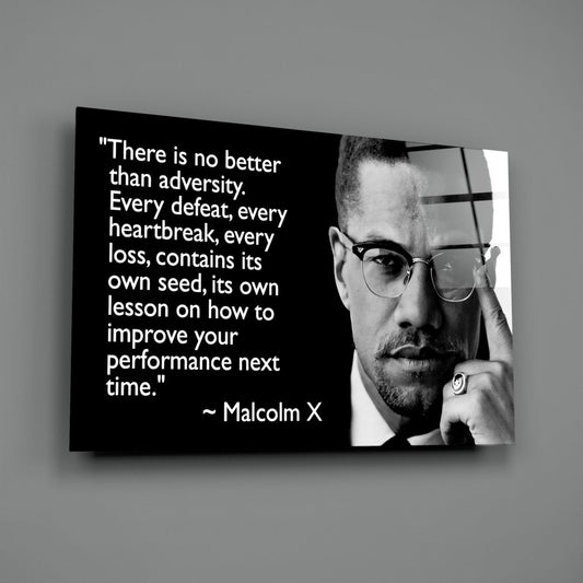 Black and white portrait of man with glasses on glass wall art displaying Malcolm X quote about adversity, mounted on gray wall.