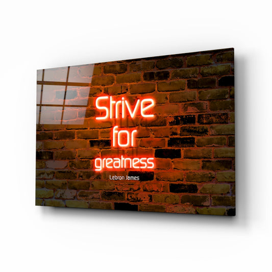 Angled view of glass wall art displaying red neon text "Strive for greatness" with "Lebron James" attribution against exposed brick background.