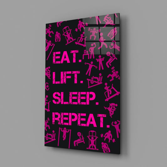 Angled perspective of black glass wall art panel with hot pink text reading "EAT. LIFT. SLEEP. REPEAT." surrounded by fitness pictograms.