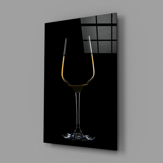 Angled view of glass wall art panel displaying elegant white wine glass with golden liquid against black background, window grid visible at top right.