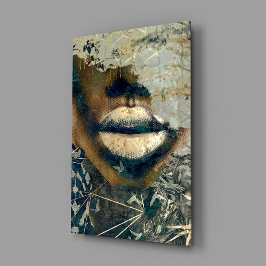Close-up view of glass wall art displaying a stylized face with golden lips, botanical elements, and layered collage textures in cream, teal, and brown tones.