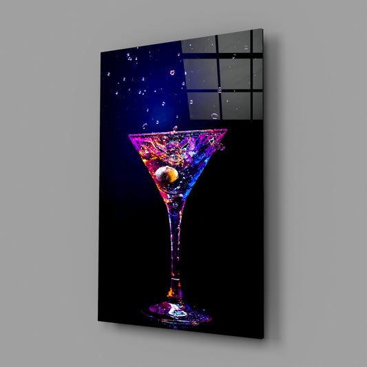 Neon purple and magenta martini glass with splashing liquid and olive displayed as framed wall art mounted at an angle against gray background.