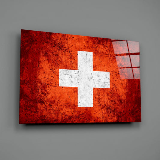 Swiss flag glass wall art with white cross on bright orange-red scratched surface, displayed at an angle against gray background.