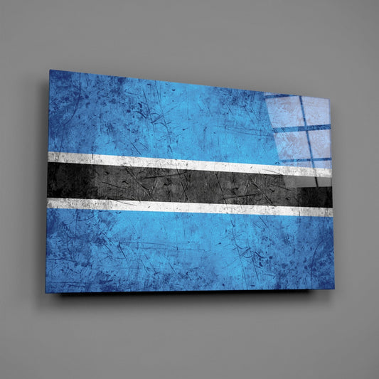 Botswana flag glass wall art displayed at an angle against a gray wall, showing blue, white, and black horizontal stripes with a weathered texture.