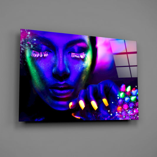 Glass wall art displaying a neon-lit woman's face in vibrant purple, blue, and green with glowing gemstones cascading from her hand, mounted on gray wall.