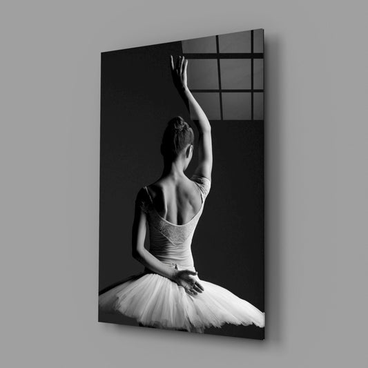Black and white glass wall art depicting a ballerina from behind, seated in a tutu, with arm raised toward a gridded window.