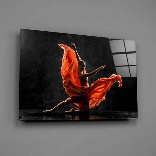 Angled view of black glass wall art displaying a dancer in flowing orange dress against dark background, mounted on gray wall.
