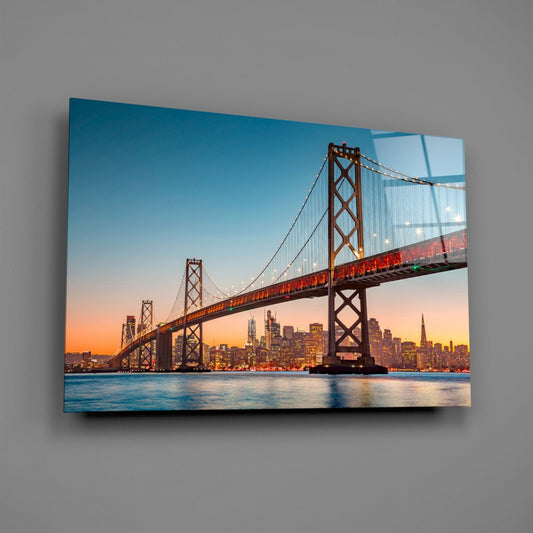 San Francisco Bay Bridge at sunset mounted on gray wall as illuminated glass art panel with city skyline.
