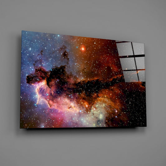 Angled view of glass wall art displaying an orange and pink nebula with stars, mounted on gray wall with visible frame edge.