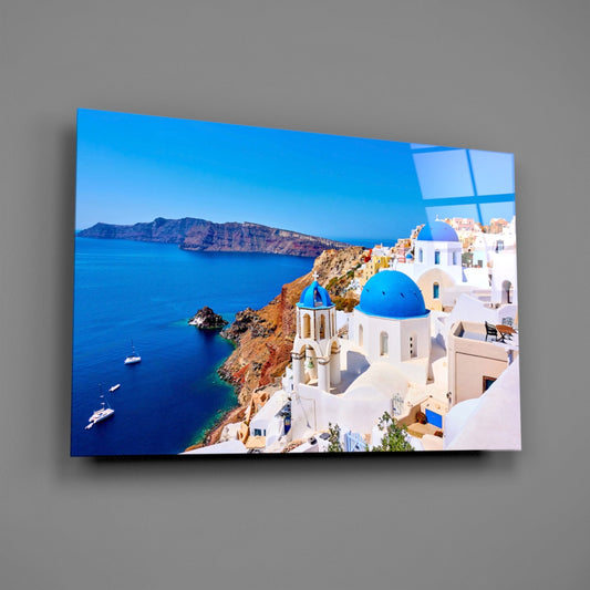 Glass wall art panel displaying Santorini's iconic white buildings with blue dome church overlooking turquoise caldera waters and distant volcanic island.