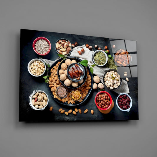 Overhead view of colorful bowls containing assorted nuts, seeds, and berries arranged on a dark slate surface with white cloth, displayed as wall art on gray background.