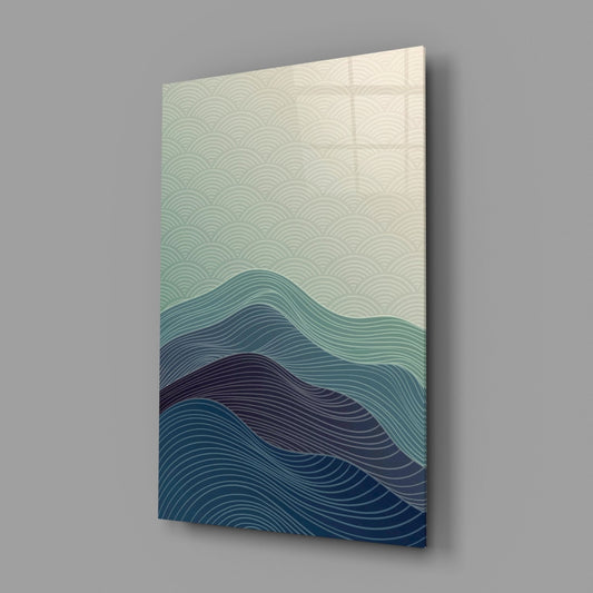 Angled view of a glass wall art panel displaying layered wave lines in cream, teal, and navy blue, mounted on gray background.