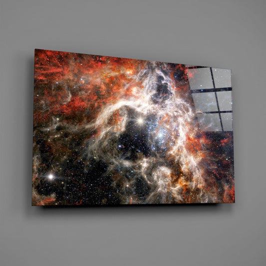 Glass wall art panel displaying a fiery nebula with red, orange, and white cosmic gas clouds against black space, mounted at an angle on gray wall.