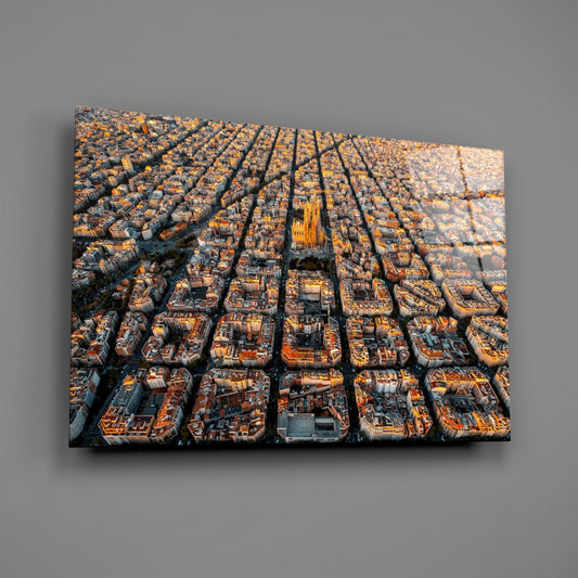 Aerial photograph on glass wall art showing Barcelona's geometric urban grid bathed in golden sunlight, with a cathedral visible in the center.