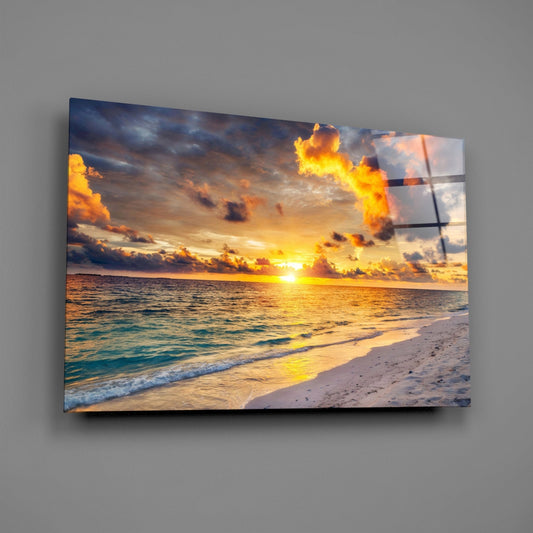 Framed glass wall art displaying a golden sunset over a beach with turquoise waves and dramatic orange clouds.
