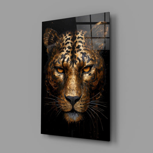 Angled view of golden bronze leopard face glass wall art with amber eyes on black background, mounted on gray wall.